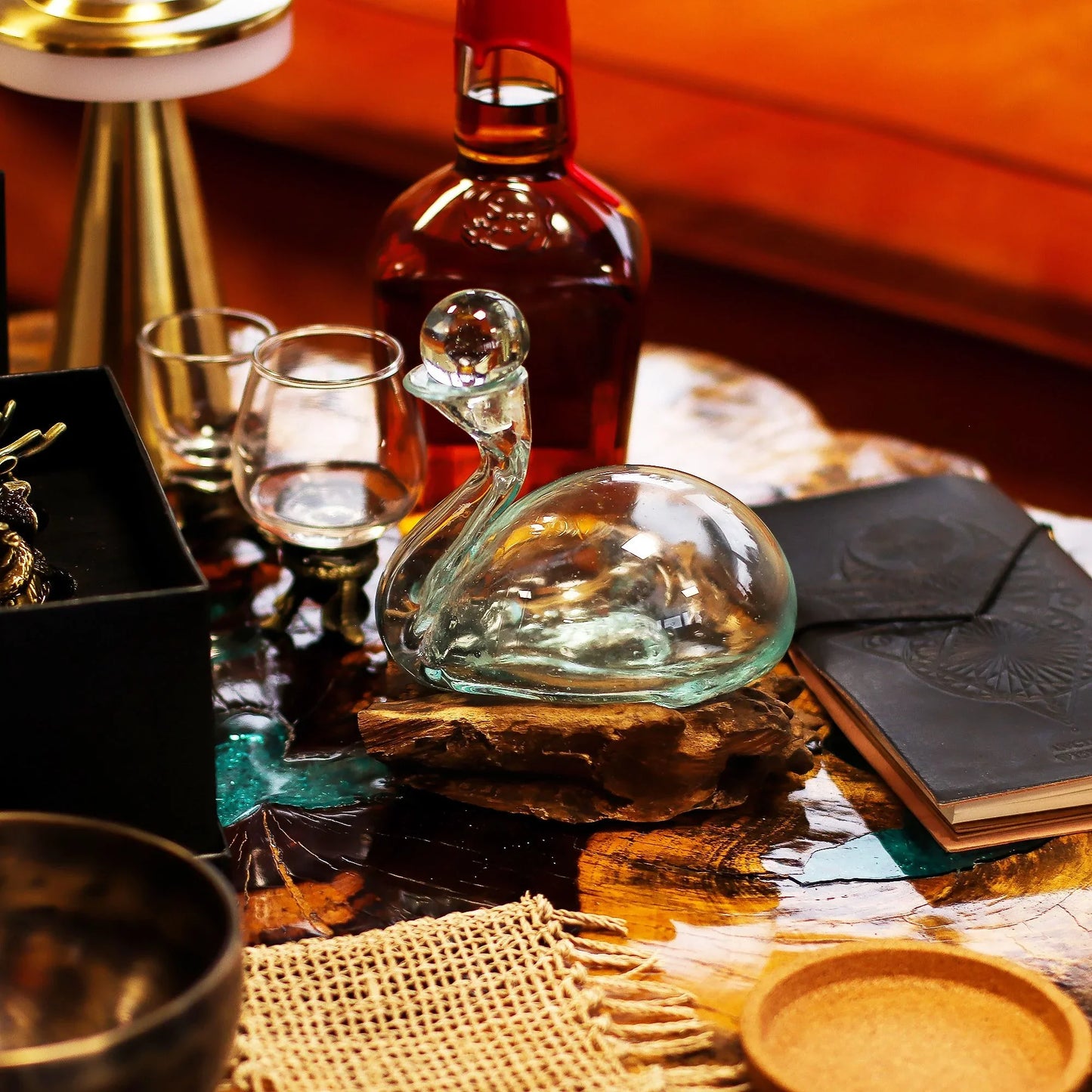 Elegant glass swan decor on wood table with bottle, glasses, and leather notebook