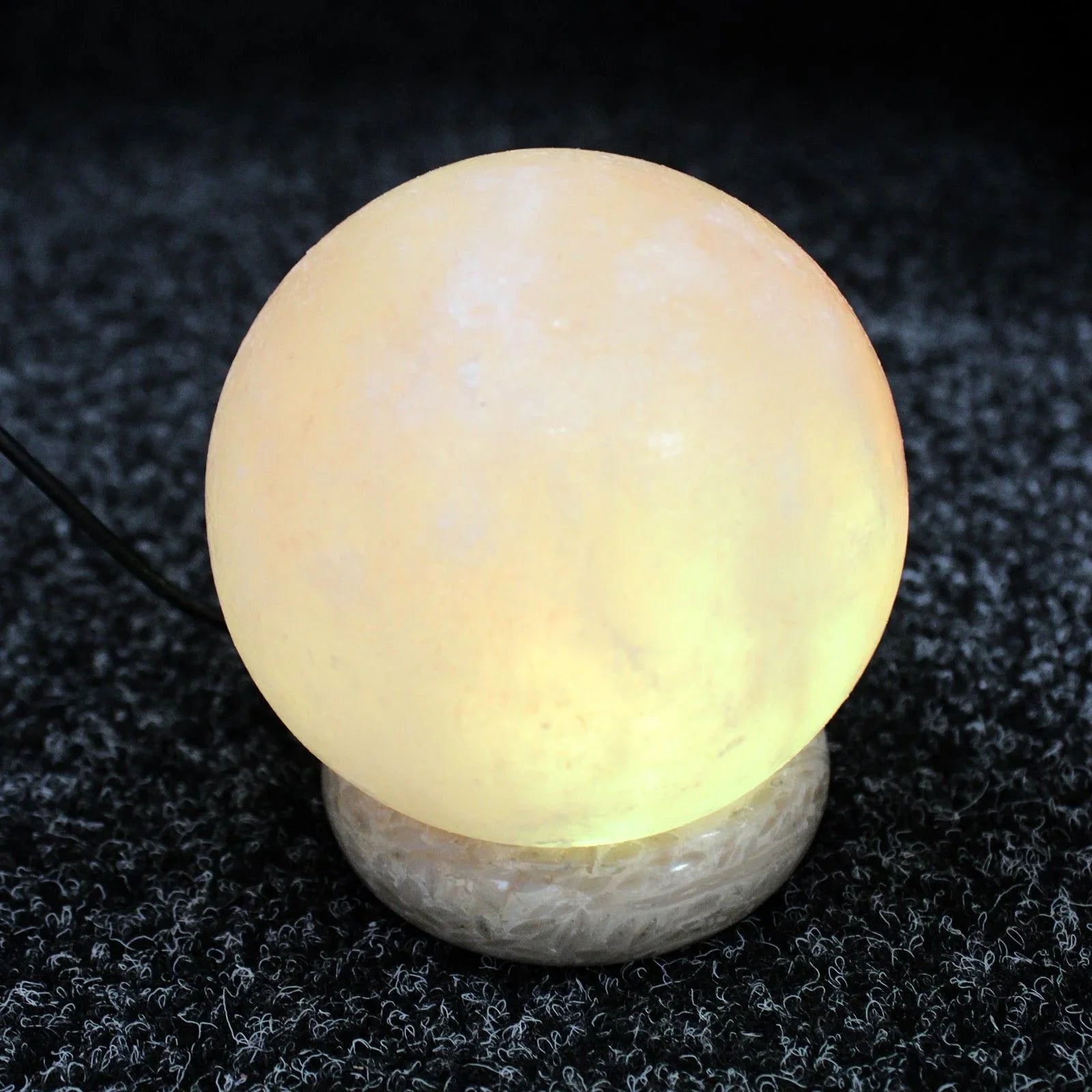 Round Himalayan salt lamp glowing on textured dark surface