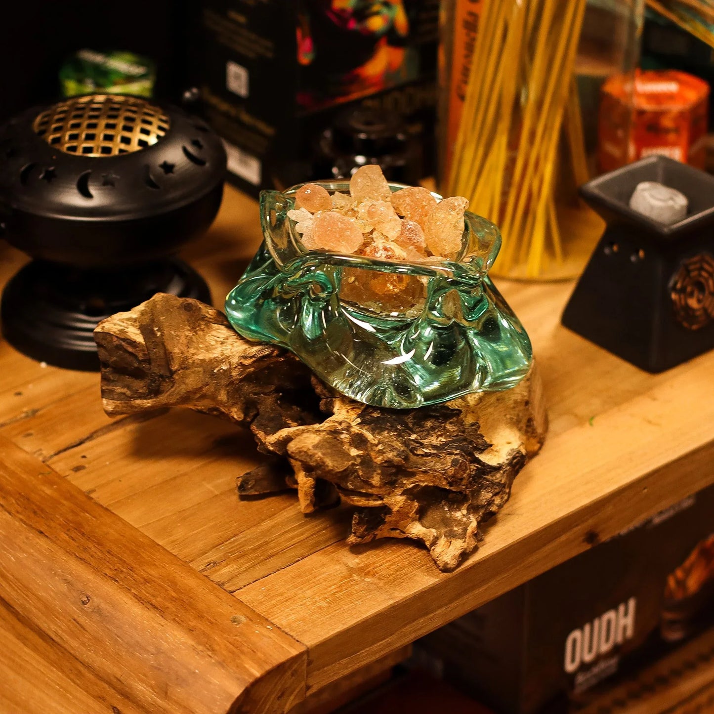 Glass bowl of amber incense resin on driftwood, with incense burners and sticks nearby
