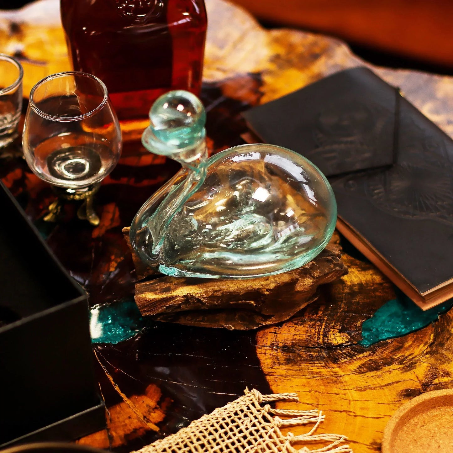 Hand-blown glass decorative swan on wooden base beside whiskey glasses and leather notebook