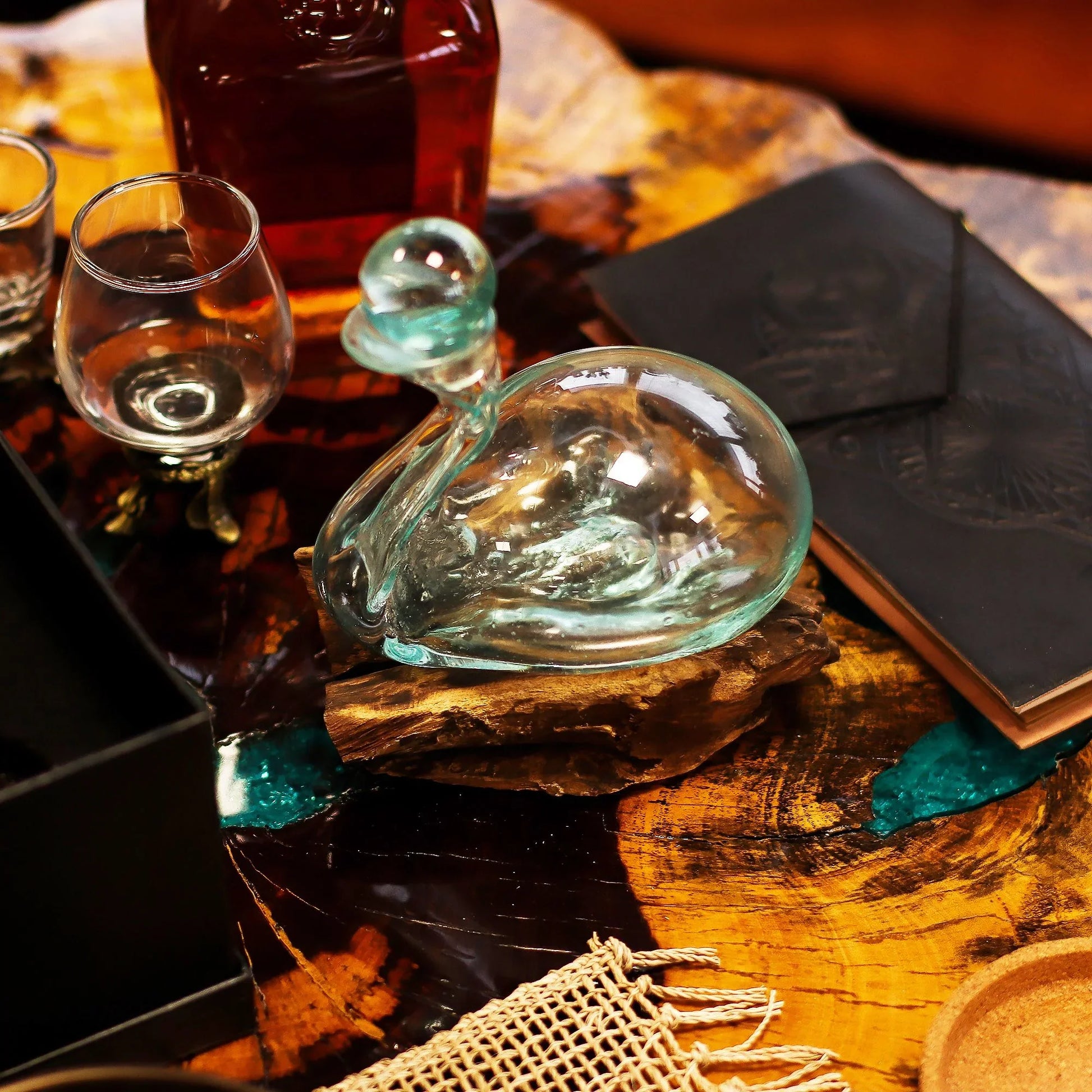 Hand-blown glass decorative swan on wooden base beside whiskey glasses and leather notebook